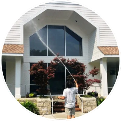 Person pressure washing a tall building exterior in Wilmington, NC, near landscaped shrubs and large windows.