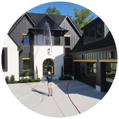 Worker performing pressure washing on a modern house facade in Wilmington, NC, using a high-pressure hose on the upper story.