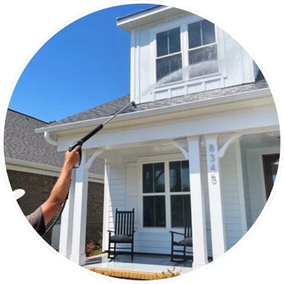 Person using a pressure washing tool on a two-story home's exterior, focusing on upper windows. House located in Wilmington, NC.