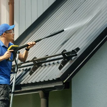 Roof Cleaning Services Person in blue uses a pressure washer to clean a metal roof. Ideal for pressure washing Wilmington NC needs.