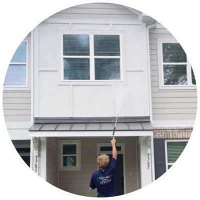 Person pressure washing the exterior of a two-story house in Wilmington, NC, cleaning upper windows and panels.