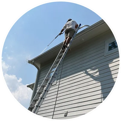 Person on ladder pressure washing house siding under clear sky; pressure washing Wilmington NC.